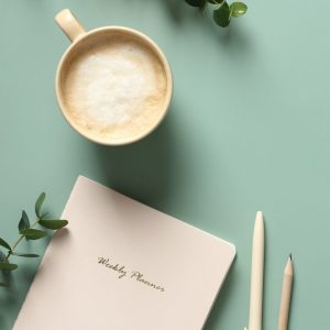 Modern home office desk table with paper notebook, cup of coffee, pen, pencil and eucalyptus leaves on green background. Minimalist style Modern home office desk table with paper notebook, cup of coffee, pen, pencil and eucalyptus leaves on green background. Minimalist style